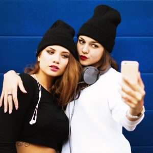 Two teenage girls friends in hipster outfit outdoors make selfie on a phone.